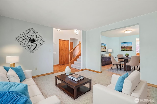 living area featuring baseboards, stairway, and light colored carpet