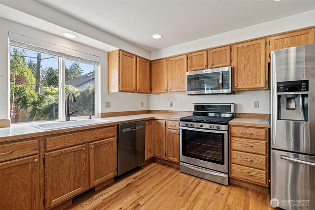 kitchen with stainless steel appliances, a sink, recessed lighting, light countertops, and light wood-style flooring