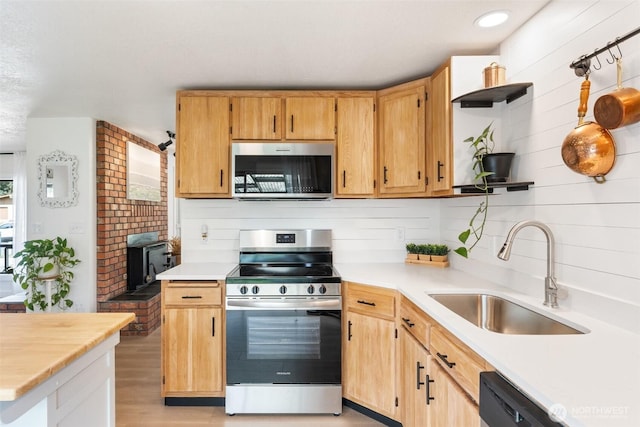 kitchen with appliances with stainless steel finishes, a sink, light countertops, light wood finished floors, and open shelves