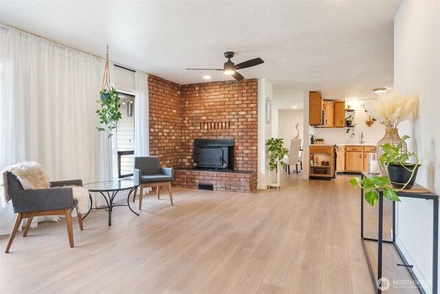 living room with a wood stove, ceiling fan, and light wood-type flooring