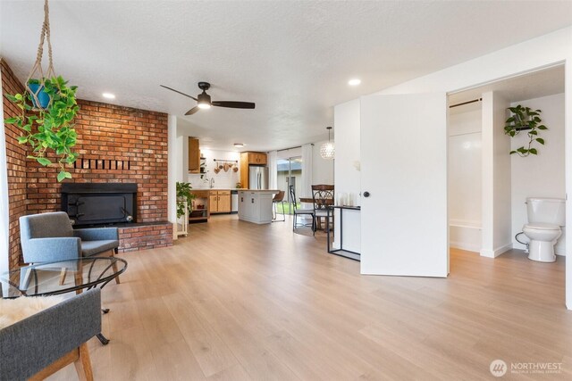 living area with light wood-style floors, ceiling fan, a brick fireplace, baseboards, and recessed lighting