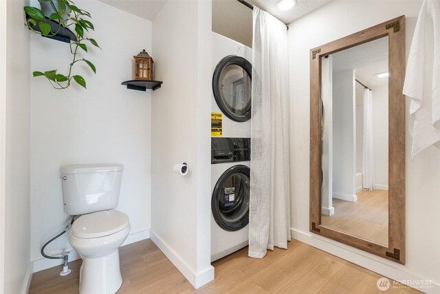 bathroom featuring stacked washer / drying machine, wood finished floors, toilet, and baseboards