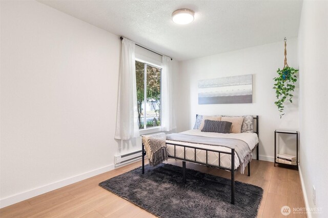 bedroom with wood finished floors, a baseboard radiator, and baseboards