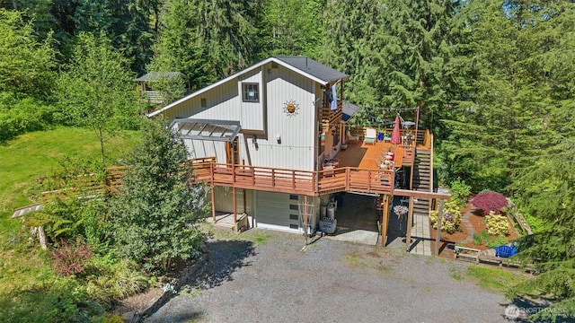 rustic home featuring a forest view, a deck, gravel driveway, and stairway