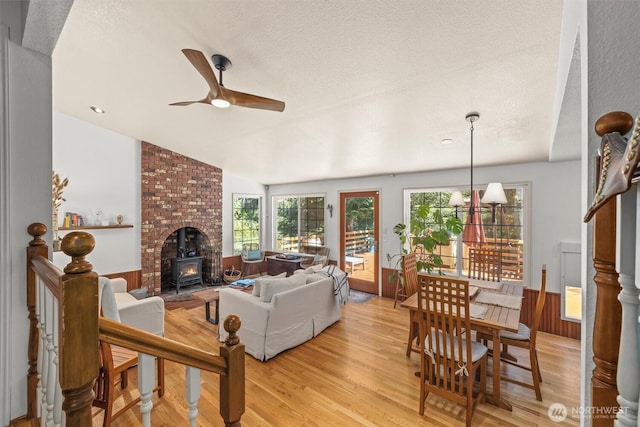 living area with a wood stove, a ceiling fan, light wood-style floors, lofted ceiling, and a textured ceiling