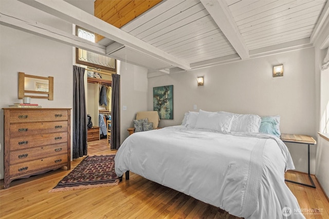 bedroom with beamed ceiling, light wood-style floors, a walk in closet, a closet, and wood ceiling