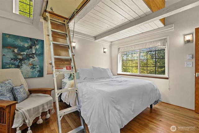 bedroom with multiple windows, wood finished floors, and beamed ceiling