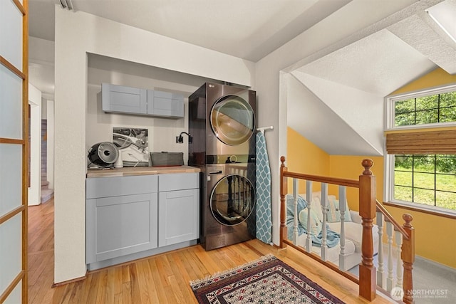 laundry area with stacked washer / drying machine and light wood-type flooring