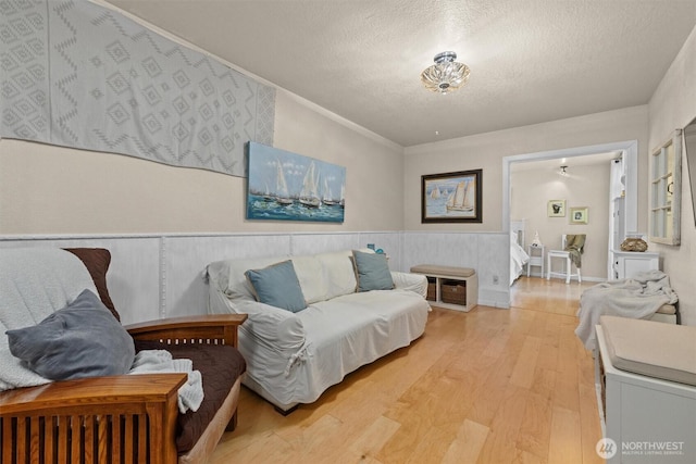 living room featuring a textured ceiling, light wood-style flooring, and a wainscoted wall