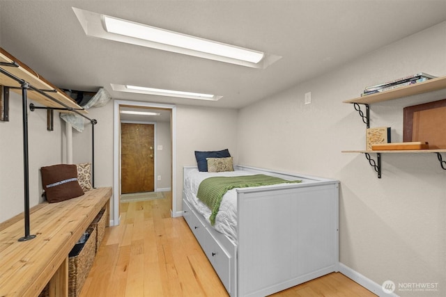 bedroom with light wood finished floors, a skylight, and baseboards