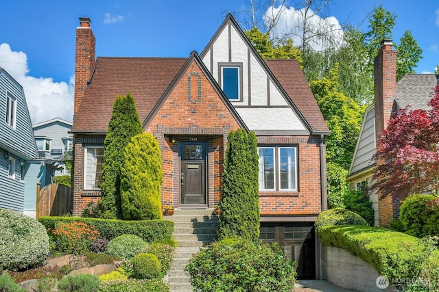 english style home featuring brick siding, a chimney, roof with shingles, and stucco siding