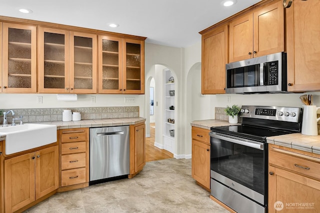 kitchen with appliances with stainless steel finishes, a sink, arched walkways, recessed lighting, and tile countertops