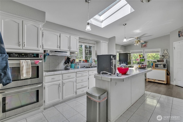 kitchen with light tile patterned floors, a skylight, tile counters, white cabinets, and appliances with stainless steel finishes