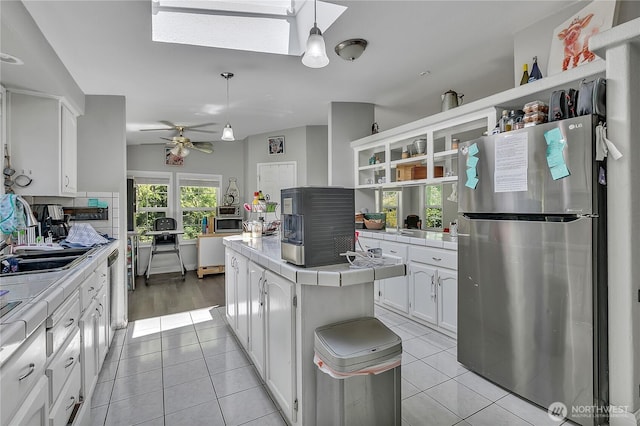 kitchen with light tile patterned floors, freestanding refrigerator, a skylight, tile counters, and white cabinetry