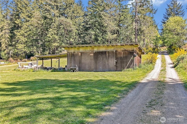view of pole building with a wooded view, driveway, and a lawn
