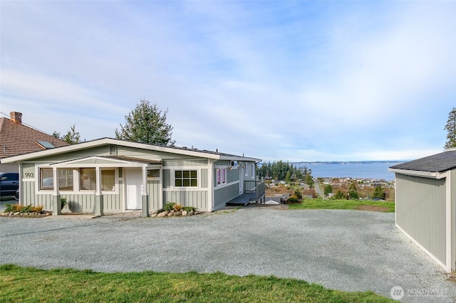 view of front of house with board and batten siding, a porch, a water view, and gravel driveway