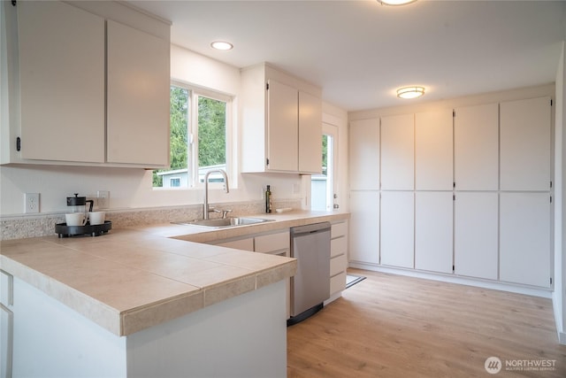 kitchen featuring a sink, recessed lighting, light wood finished floors, light countertops, and stainless steel dishwasher