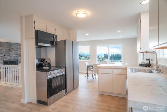 kitchen with a sink, stainless steel appliances, tile counters, and plenty of natural light