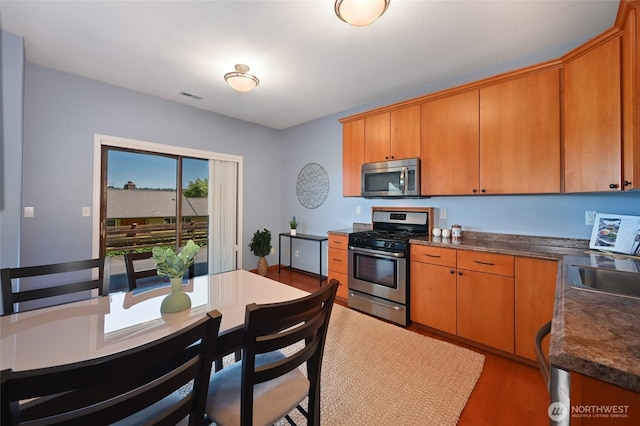 3911 NE 158th Ln, Lake Forest Park, WA 98155 - kitchen featuring appliances with stainless steel finishes, dark countertops, brown cabinetry, light wood-type flooring, and a sink