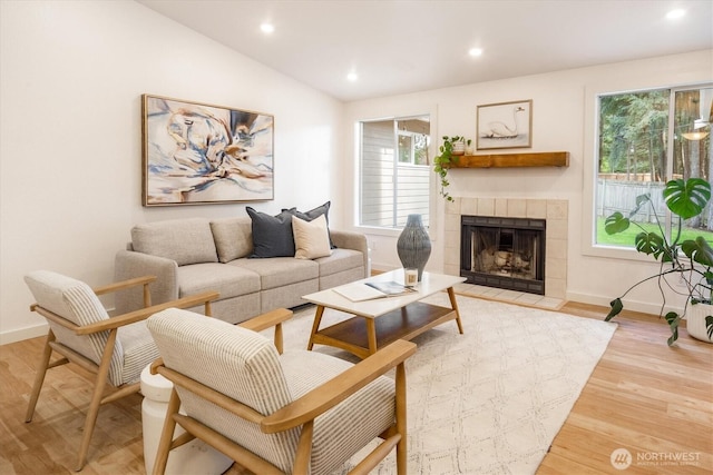 living area with light wood-type flooring, baseboards, a fireplace, lofted ceiling, and recessed lighting