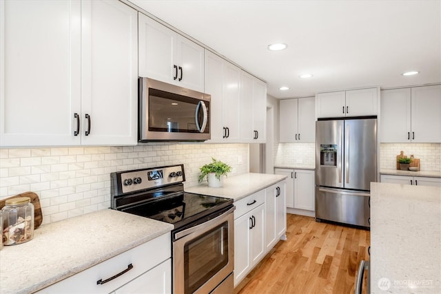 kitchen with stainless steel appliances, backsplash, white cabinets, light wood-style flooring, and light stone counters