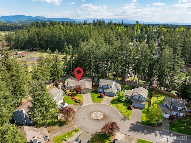 aerial perspective of suburban area featuring a mountain backdrop and a heavily wooded area