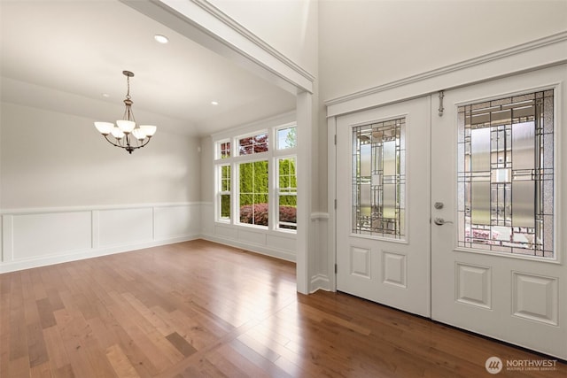 entrance foyer featuring a wainscoted wall, hardwood / wood-style floors, french doors, recessed lighting, and an inviting chandelier