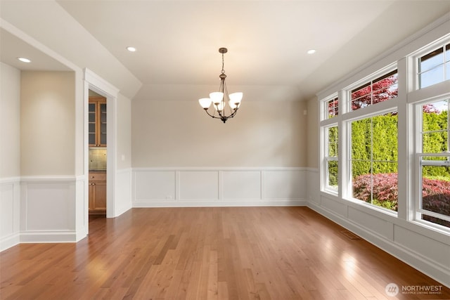 unfurnished dining area featuring wainscoting, a chandelier, light wood finished floors, and a healthy amount of sunlight