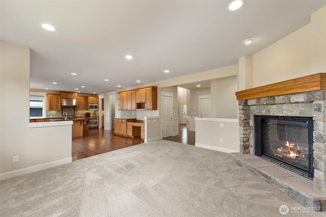 unfurnished living room with baseboards, dark carpet, a stone fireplace, and recessed lighting
