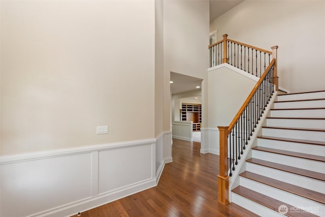 staircase with a wainscoted wall and wood finished floors
