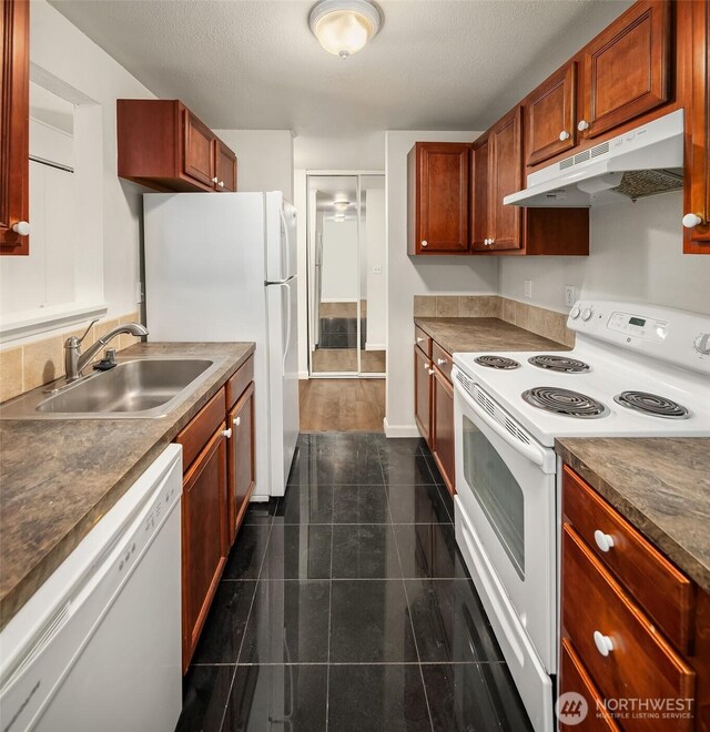 kitchen featuring white appliances, under cabinet range hood, a sink, dark tile patterned floors, and dark countertops