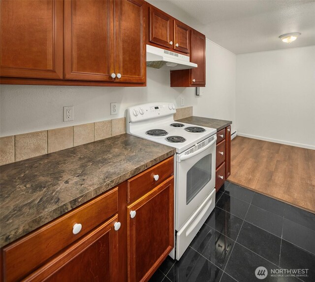 kitchen with electric stove, under cabinet range hood, dark countertops, dark tile patterned flooring, and a baseboard heating unit