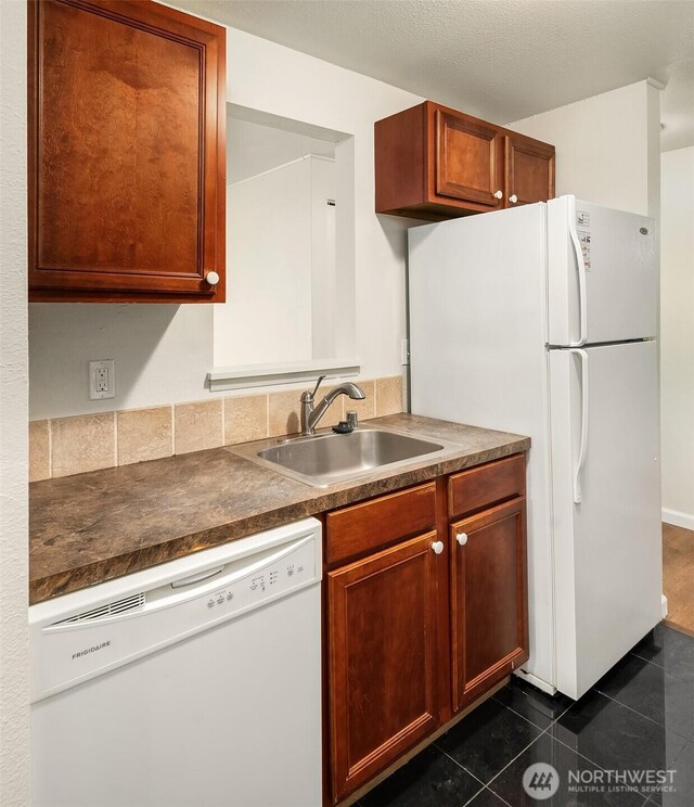 kitchen featuring white appliances, a sink, dark countertops, and dark tile patterned floors