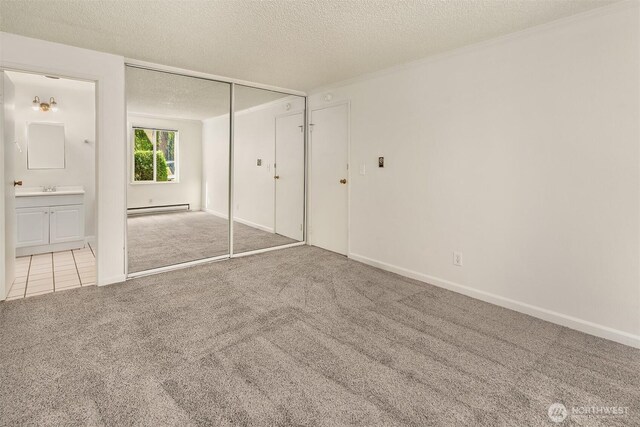 unfurnished bedroom featuring baseboard heating, carpet flooring, a textured ceiling, a closet, and connected bathroom