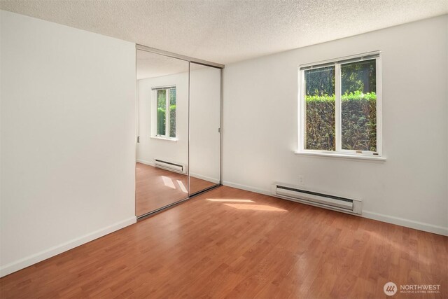 unfurnished bedroom with a baseboard heating unit, wood finished floors, a textured ceiling, and baseboards