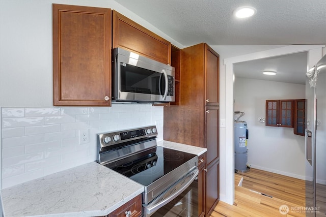103 Madison St, Ryderwood, WA 98581 - kitchen featuring appliances with stainless steel finishes, water heater, light wood finished floors, light stone counters, and decorative backsplash