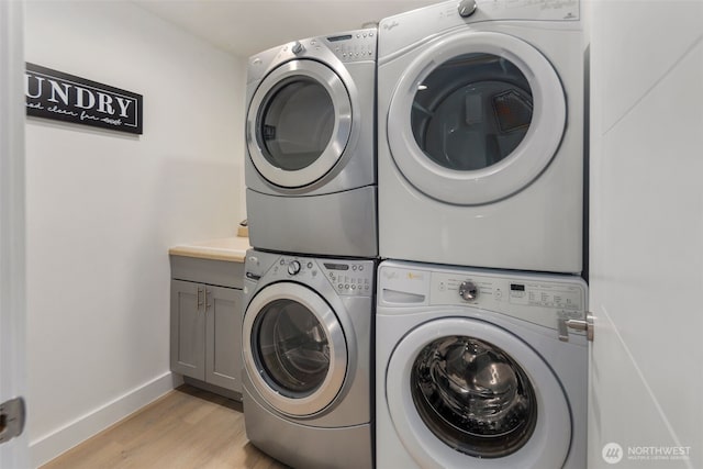 laundry area featuring stacked washer / dryer, cabinet space, light wood-style flooring, and baseboards