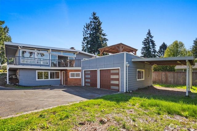 view of front of property featuring driveway, an attached garage, fence, a balcony, and an outdoor structure