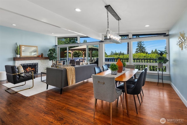 dining room with wood finished floors, a warm lit fireplace, baseboards, and recessed lighting