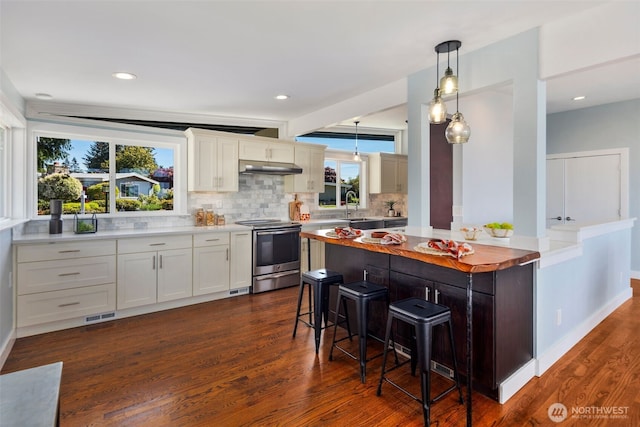kitchen with stainless steel electric range oven, a kitchen breakfast bar, decorative backsplash, dark wood finished floors, and a sink