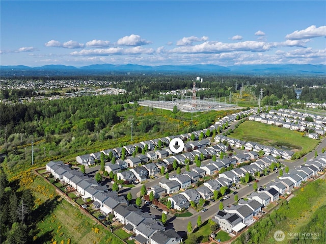 aerial view of property and surrounding area featuring a forest, a mountain backdrop, and nearby suburban area