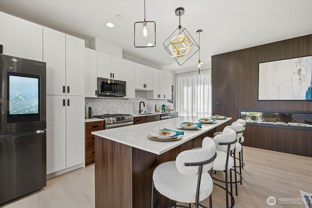 kitchen with appliances with stainless steel finishes, a sink, light countertops, a kitchen breakfast bar, and white cabinetry