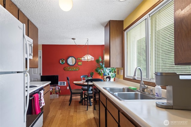 kitchen featuring white appliances, a sink, light countertops, a textured ceiling, and light wood finished floors