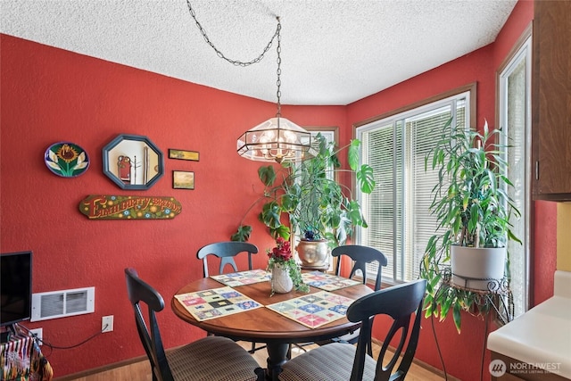 dining area featuring plenty of natural light, a textured ceiling, a chandelier, wood finished floors, and baseboards