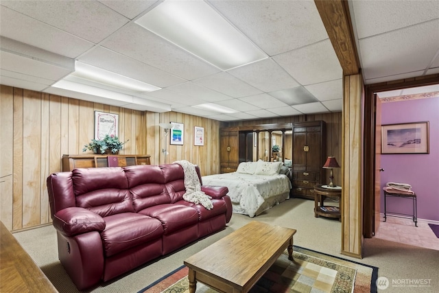 carpeted bedroom with a paneled ceiling and wood walls