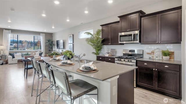 kitchen with dark brown cabinets, a sink, open floor plan, a kitchen island with sink, and appliances with stainless steel finishes