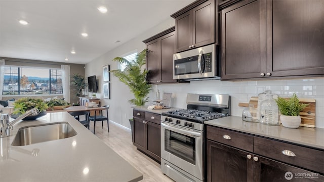 kitchen featuring a sink, dark brown cabinetry, light wood-type flooring, backsplash, and appliances with stainless steel finishes