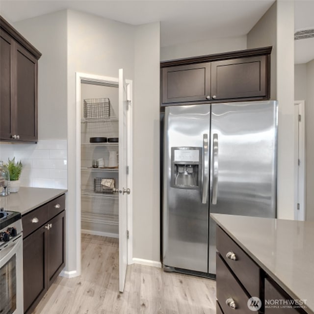 kitchen with dark brown cabinets, light wood-style floors, backsplash, light countertops, and appliances with stainless steel finishes
