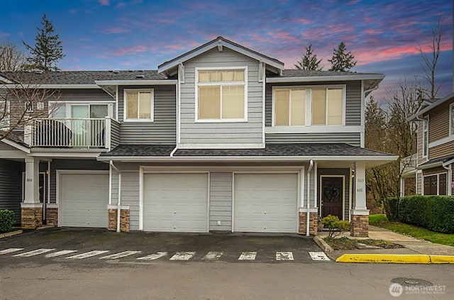 townhome / multi-family property featuring a garage, stone siding, a balcony, and asphalt driveway