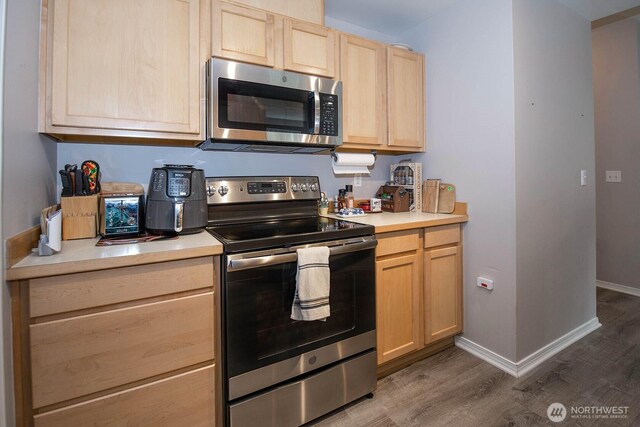 kitchen with stainless steel appliances, light brown cabinetry, wood finished floors, light countertops, and baseboards